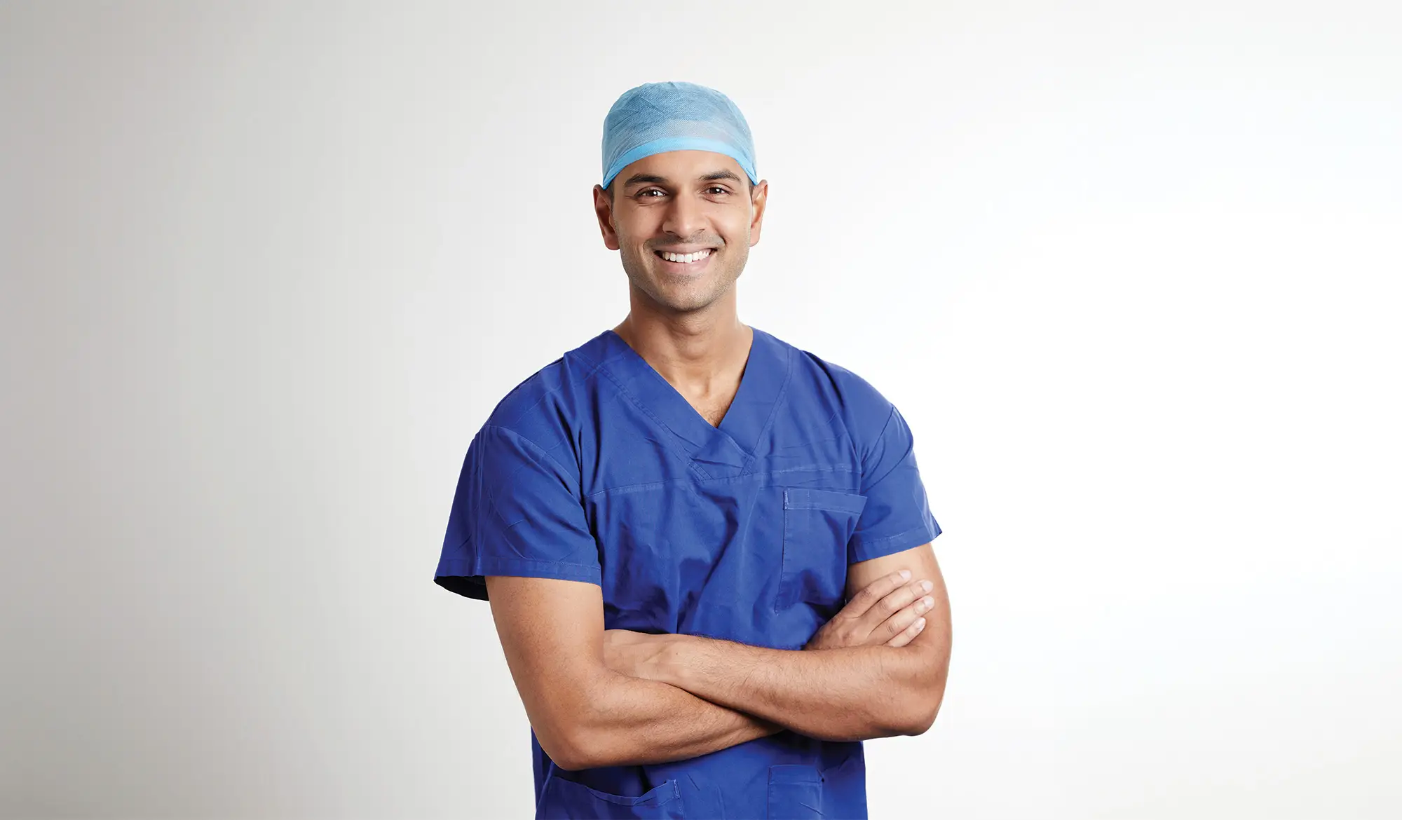 Dr Nikhil Vasan wearing medical scrubs. He stands in a confident posture and smiles at the viewer.